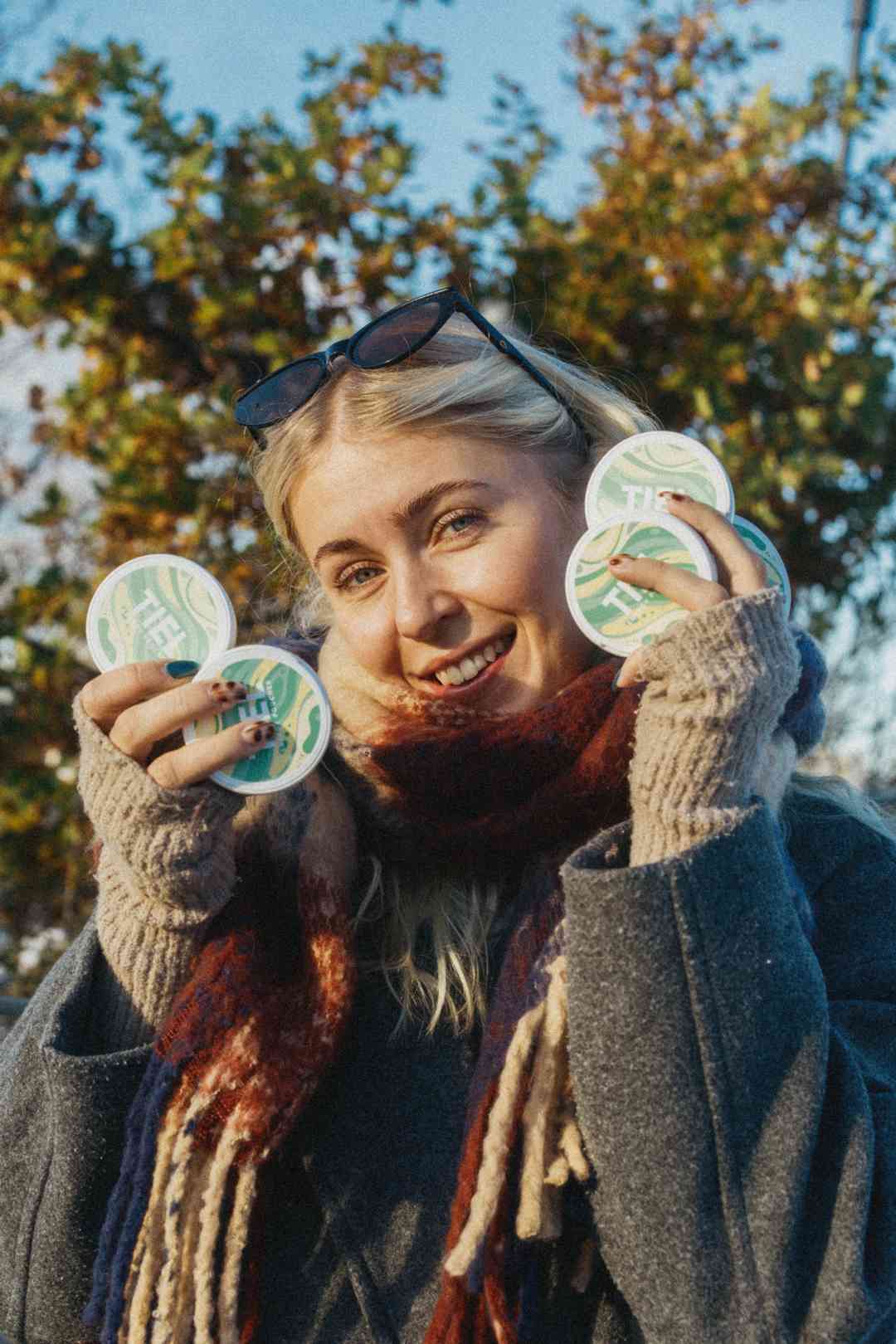 Tjej som håller upp flera dosor av TIEL energy pouches i olika smaker som del av FAQ-sektion som förklarar produkten och koffein snus alternativ