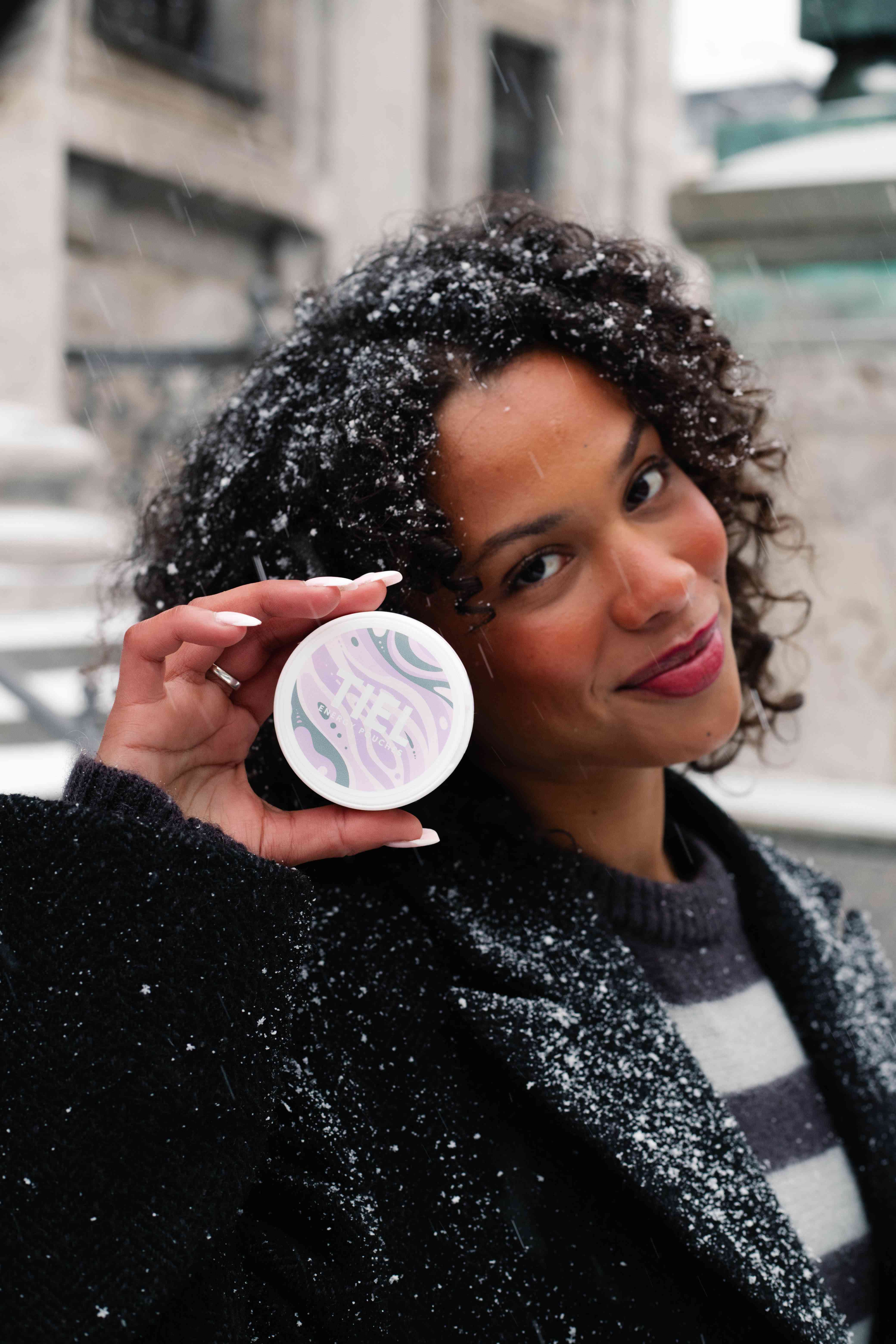 UGC-bild på tjej utomhus i snö som håller en TIEL dosa i smaken viol och lakrits – nikotinfritt snus med koffein